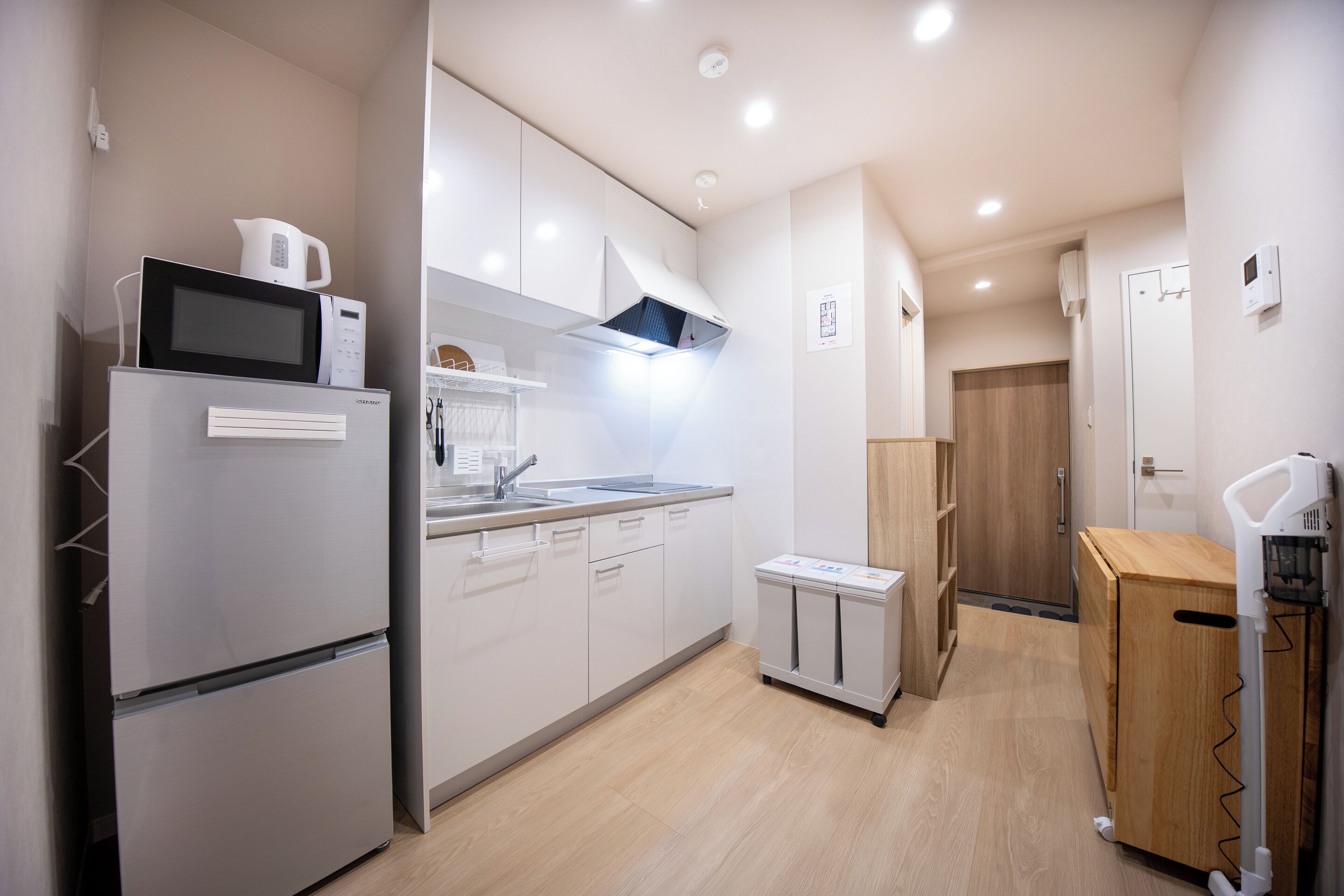 Una cucina moderna con mobili bianchi, un forno a microonde integrato e un frigorifero compatto.
