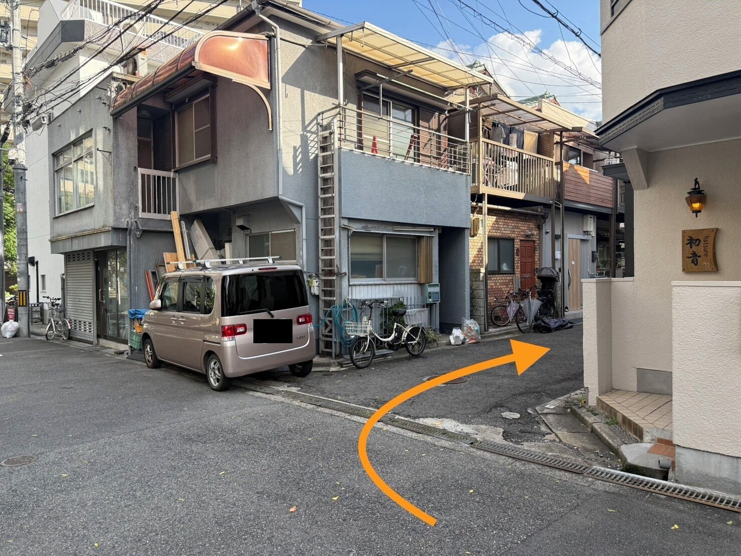 Una calle residencial con una furgoneta estacionada al lado, una bicicleta y un edificio con un letrero que dice "Hatsune".