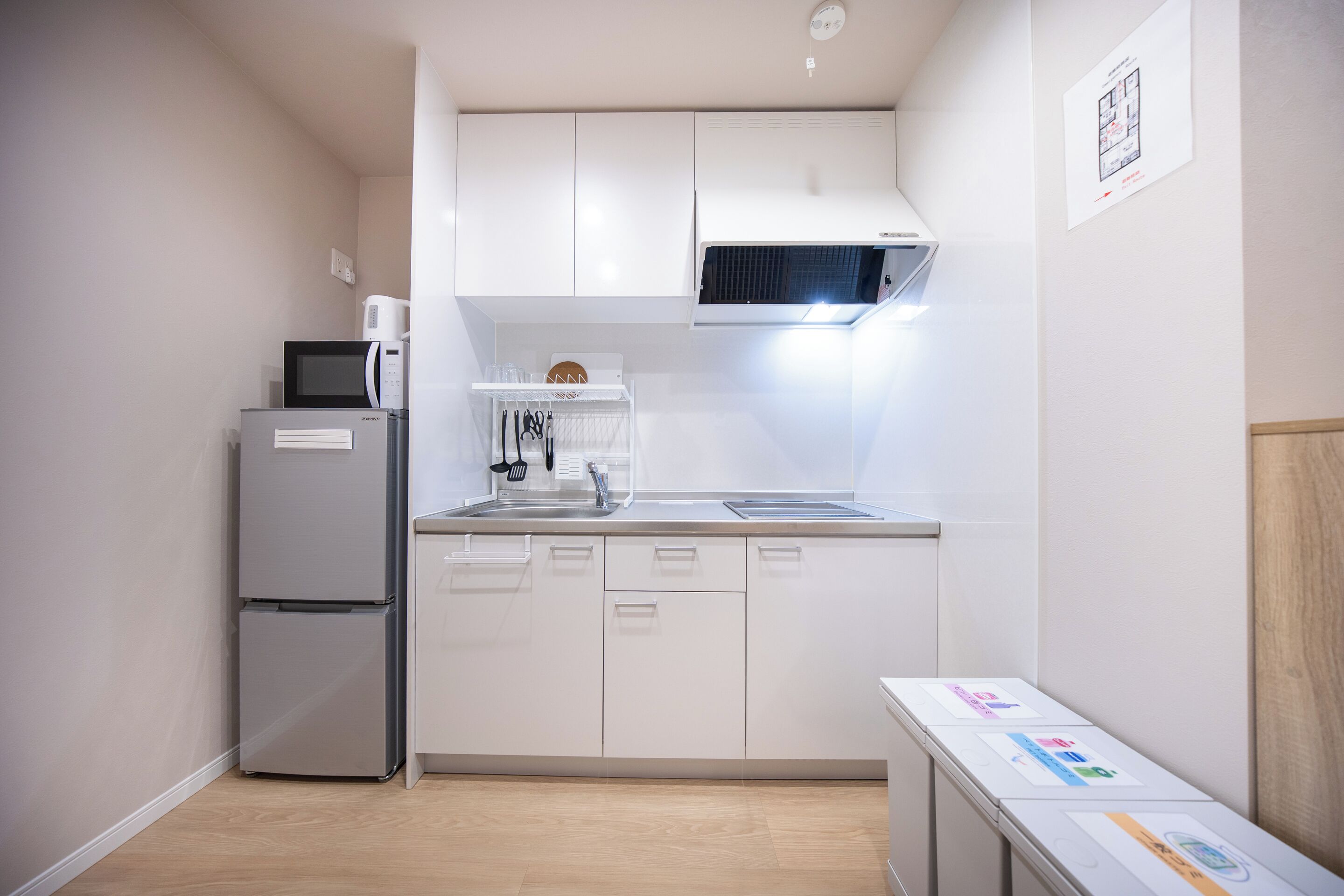 Een kleine keuken met witte kastjes, een magnetron, een koelkast en een spoelbak.