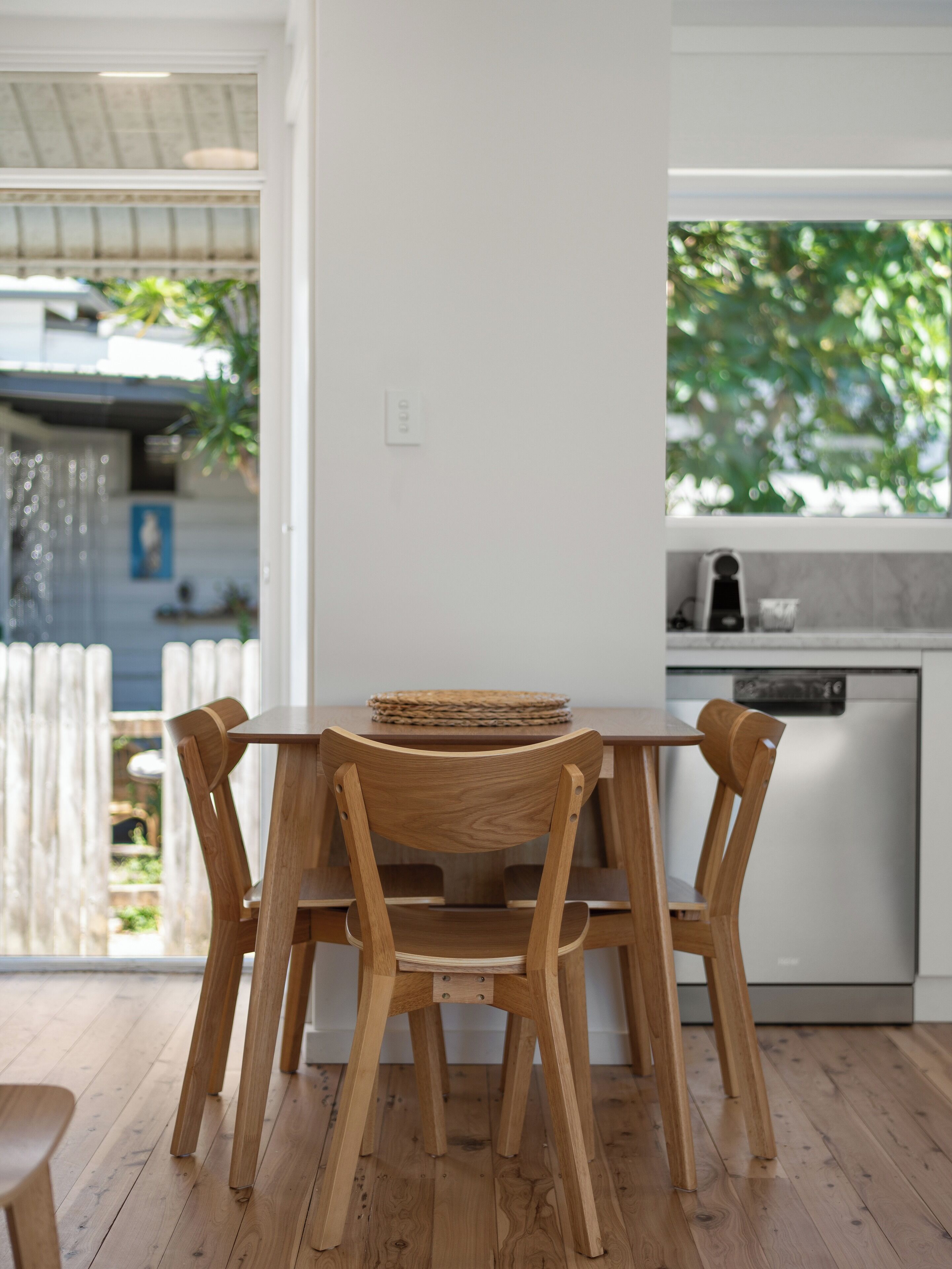 Una mesa de comedor de madera con sillas, una zona de cocina con lavavajillas y vistas a zonas verdes.