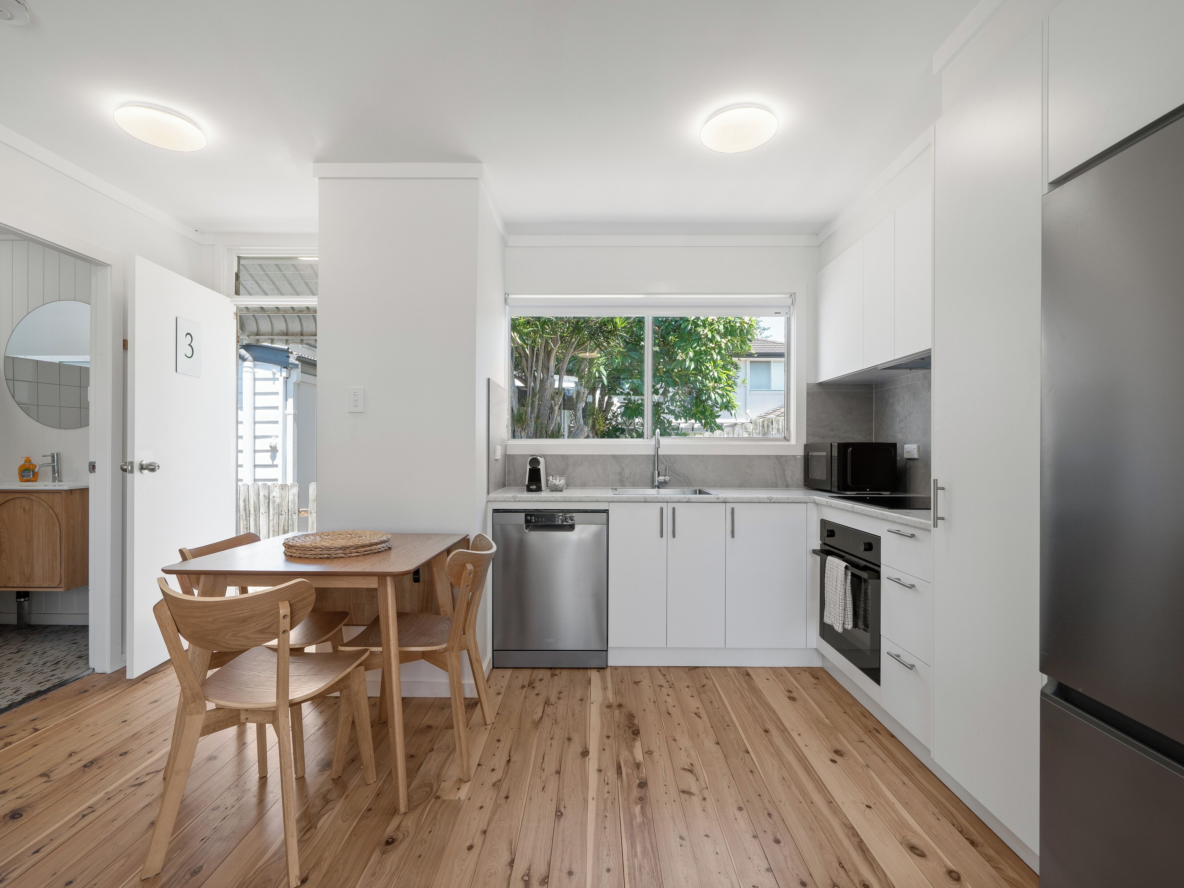 Una cocina moderna con armarios blancos, un refrigerador de acero inoxidable y una mesa de comedor de madera con sillas.