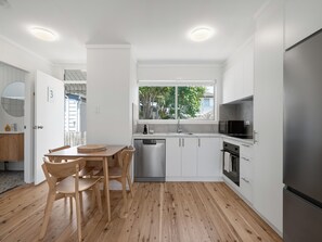 Una cocina moderna con armarios blancos, un refrigerador de acero inoxidable y una mesa de comedor de madera con sillas.