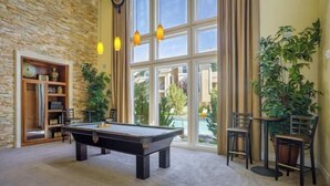 A pool table in a room with a stone wall, large windows, and potted plants. - New Trendy 1BR Apartment with Heated Pool, Gym & Minigolf (Reno)