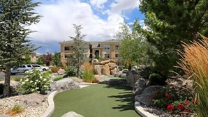 A landscaped garden with a green lawn, large rocks, and various shrubs. - New Trendy 1BR Apartment with Heated Pool, Gym & Minigolf (Reno)