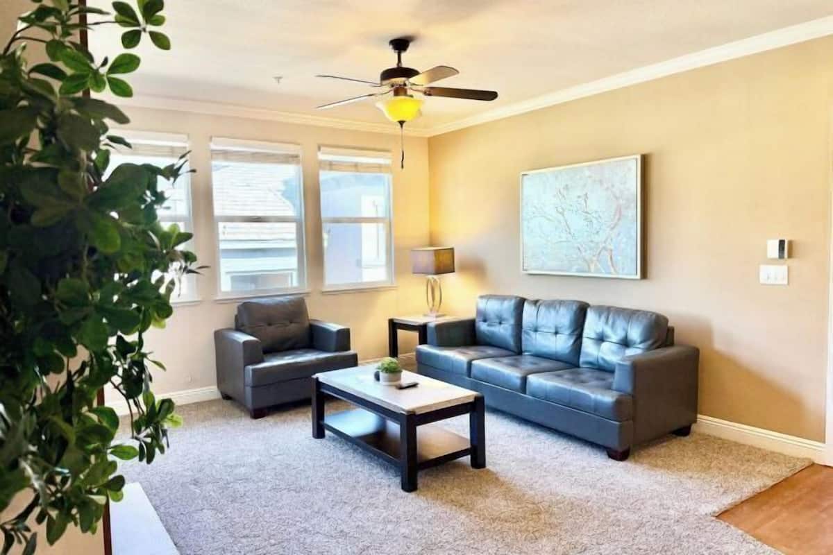A living room with a ceiling fan, two sofas, a coffee table, and a large abstract painting on the wall.