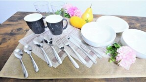 A table set with white bowls, spoons, and black mugs on a newspaper-covered placemat, accompanied by a yellow pear and pink flowers. - Nisshou House (Sapporo)