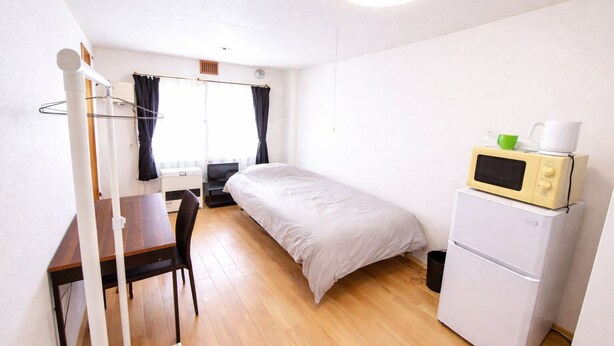 A compact room with a bed, a desk, a chair, a microwave, and a small refrigerator. - Nisshou House (Sapporo)