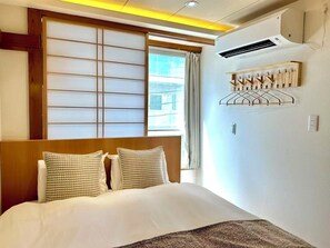 Ein Hotelzimmer mit Bett, einer verschiebbaren Shoji-Schirmwand, einer Klimaanlage und einem Wandtrockner.