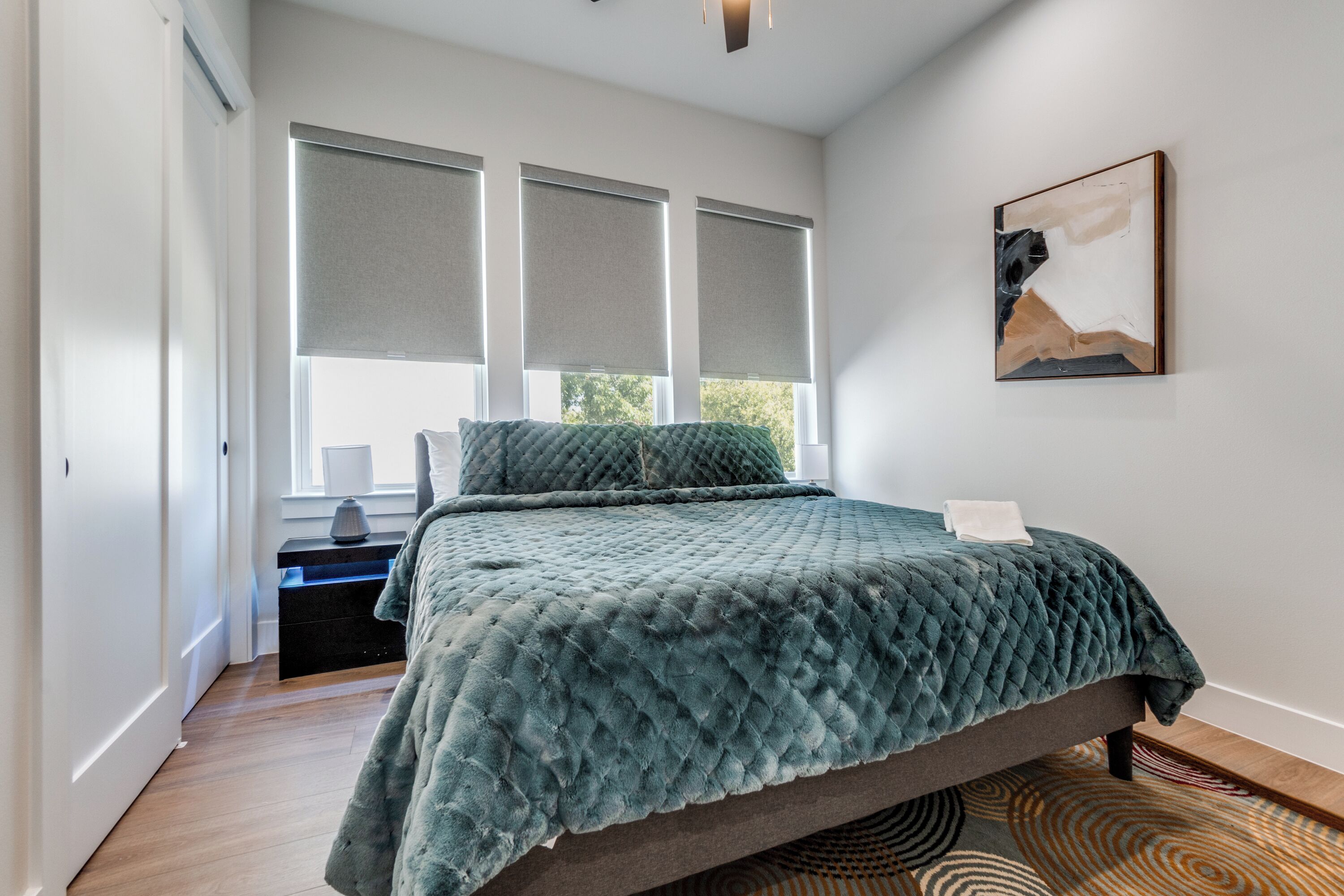 Un dormitorio con cama, mesita de noche, lámpara y un cuadro en la pared.