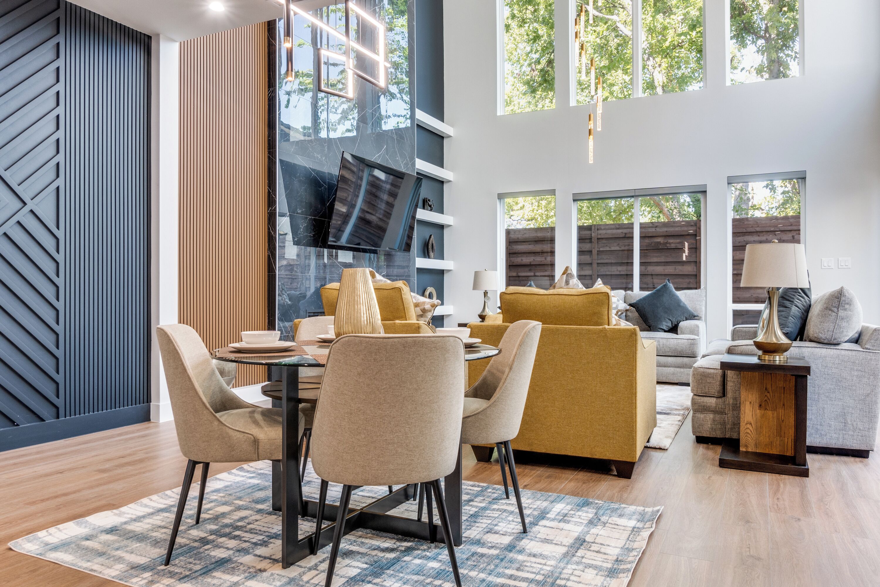 Un salon moderne comprenant un coin repas, de grandes fenêtres et un mélange de décorations en bois et en métal.