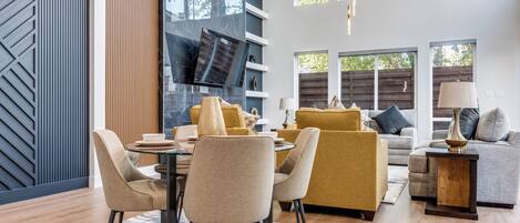 Un salon moderne comprenant un coin repas, de grandes fenêtres et un mélange de décorations en bois et en métal.