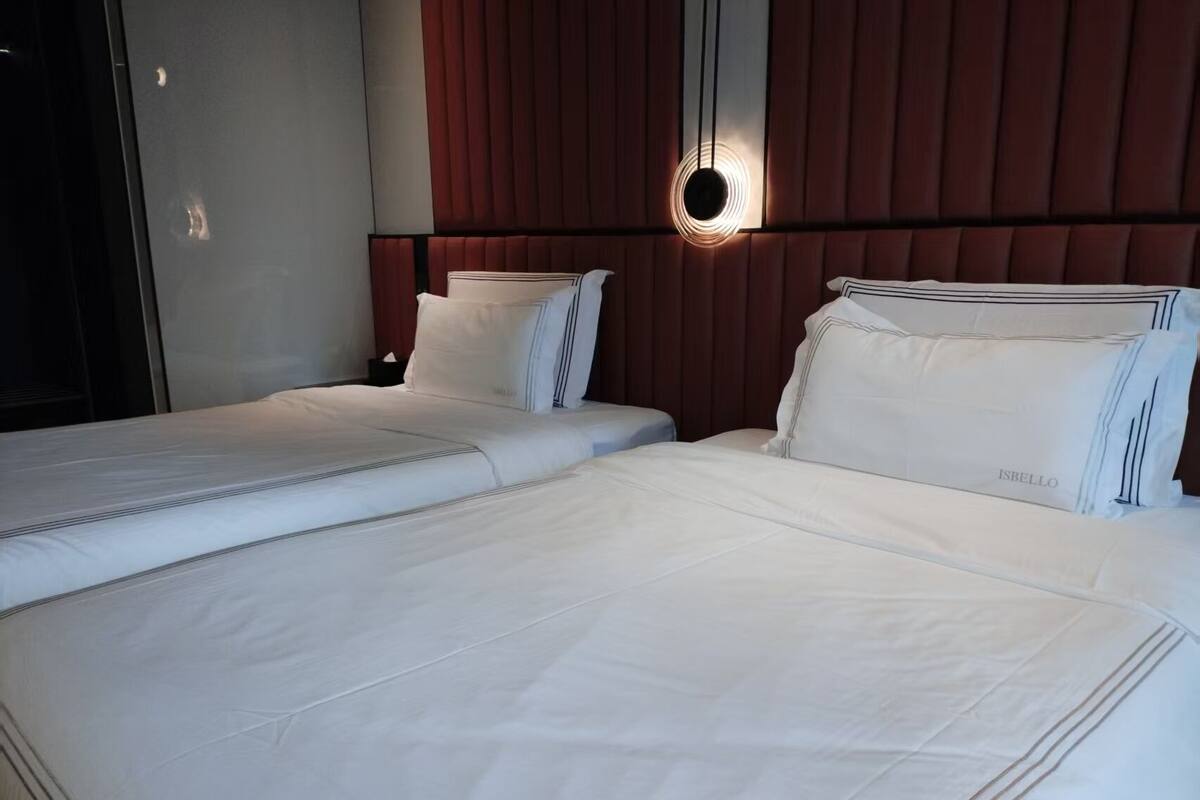 A hotel room with two beds, a modern headboard, and a wall-mounted light fixture.