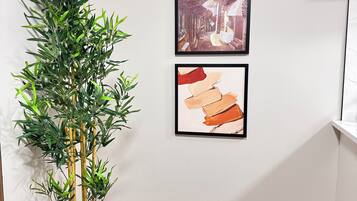 Une pièce avec une plante en bambou dans un pot noir, un plancher en bois et deux œuvres d’art encadrées accrochées au mur.