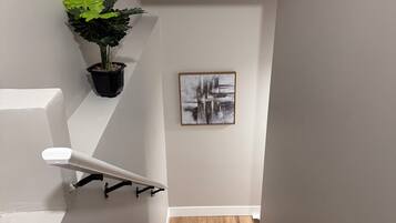 A staircase with wooden steps, white walls, a black potted plant, and a framed abstract painting.
