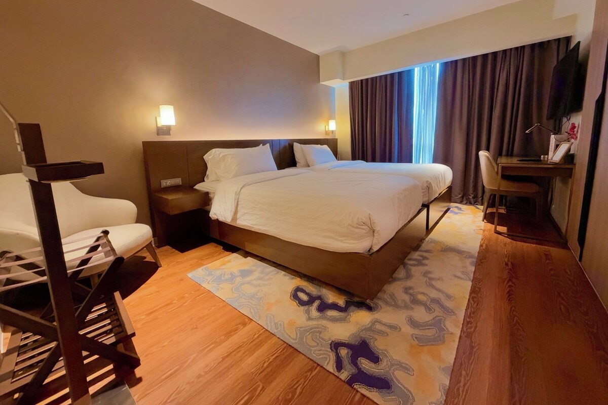 A hotel room with a large bed, bedside tables, a desk, and a chair.