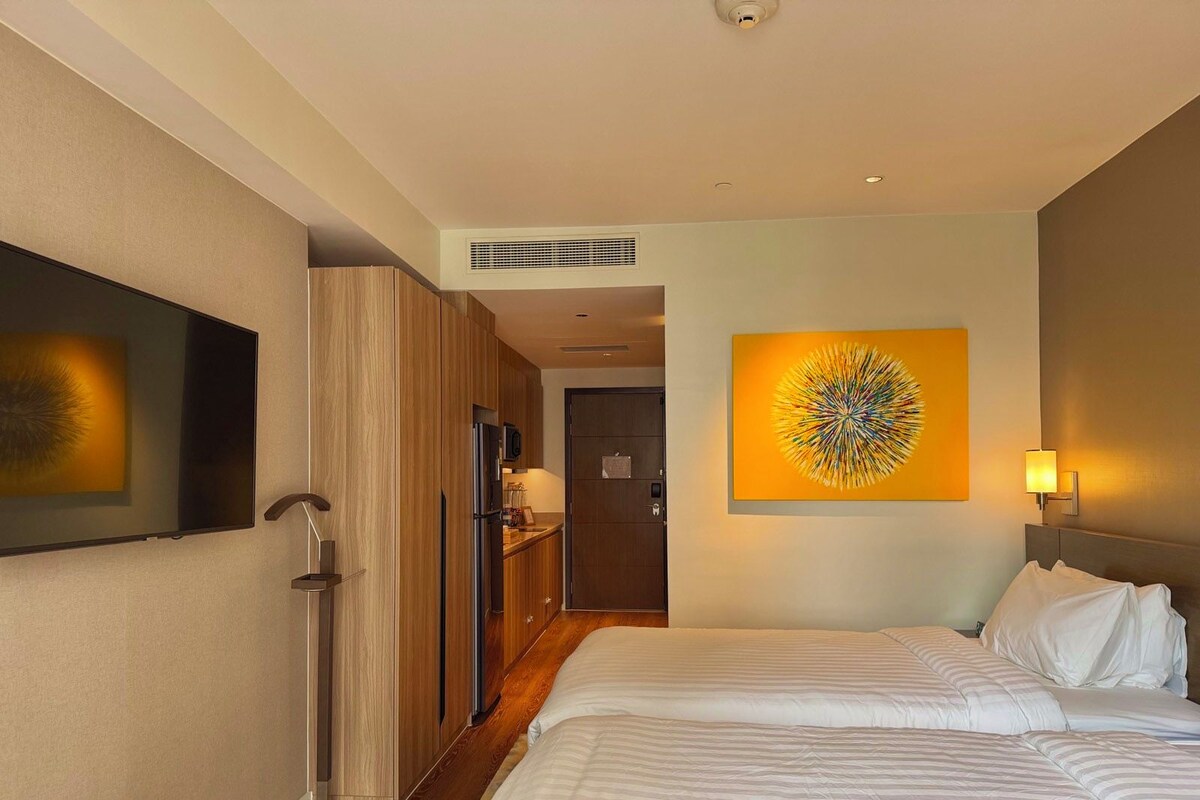 A hotel room with a bed, a television, a kitchen area, and a bathroom.