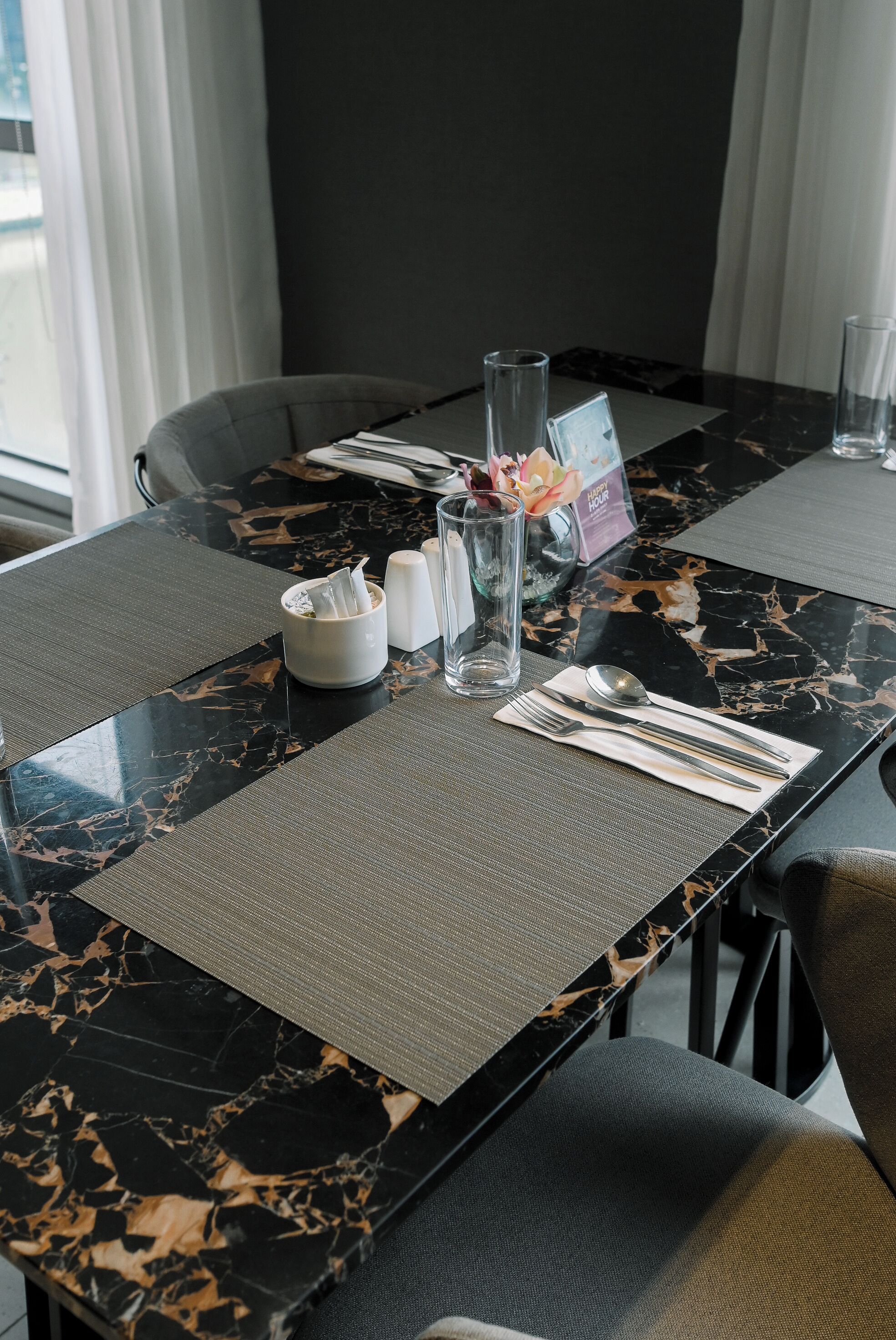 Una mesa de comedor con cubierta de mármol negro, una servilleta blanca, cubiertos, un florero de vidrio con flores y un menú.