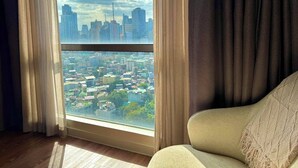 A room with a large window offering a cityscape view, a sofa, and curtains. - Hotel Residences at Acqua (Mandaluyong)