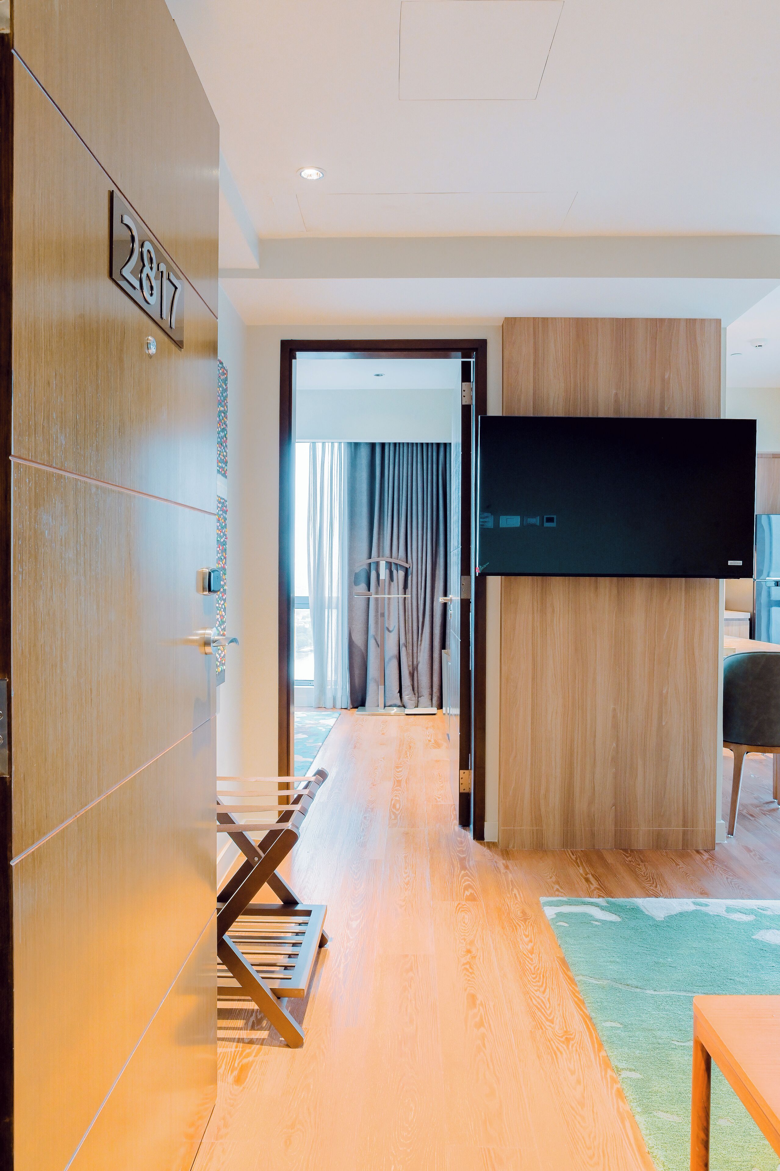 A hotel room with a wooden floor, a flat-screen TV mounted on the wall, and a door labeled "2817".
