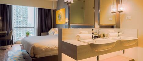 A hotel room with a large bed, a double sink vanity, a large mirror, and a view of a cityscape through the window.