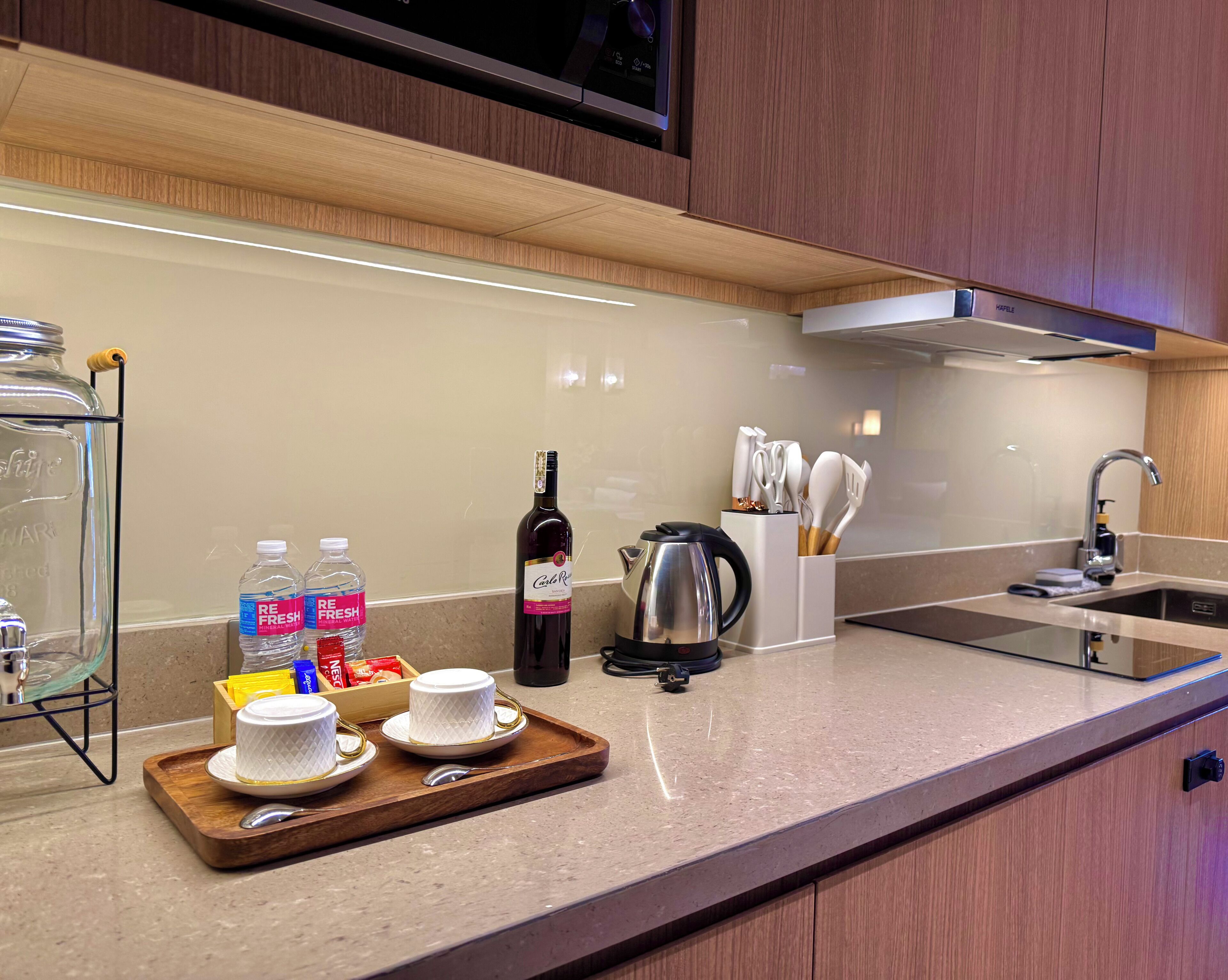 A modern kitchen with a countertop, a coffee maker, a wine bottle, and a tray with cups and a spoon.