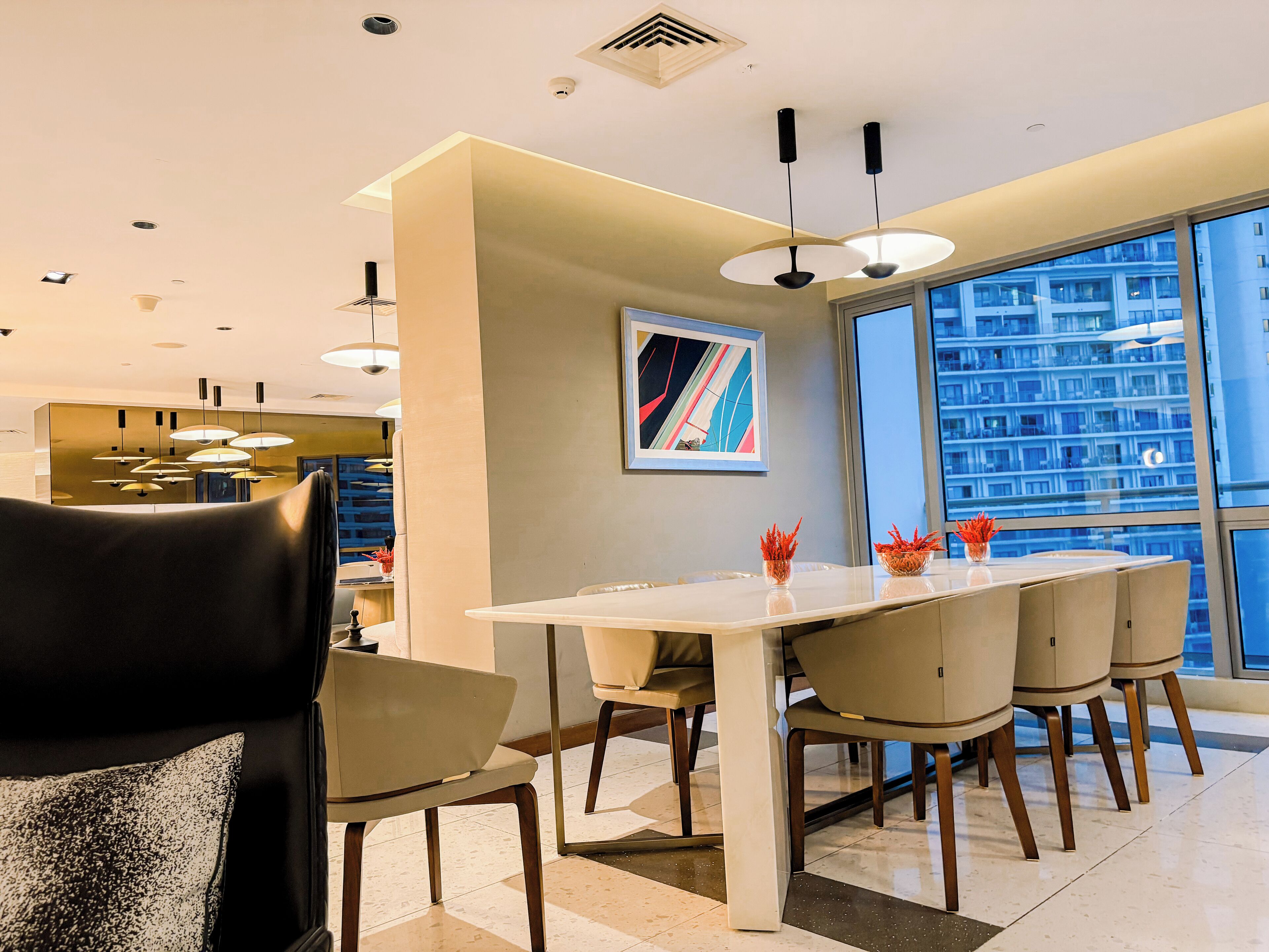 A modern dining area with a white table, beige chairs, and pendant lighting.