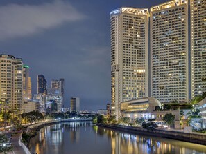 Un hotel de gran altura con varios pisos, un río en primer plano y edificios circundantes.