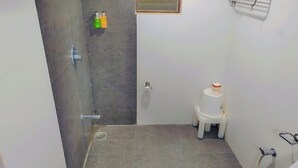 Un baño pequeño y funcional con ducha, inodoro y un estante con artículos de aseo.