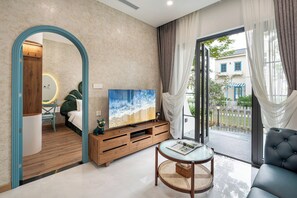 A modern living room with a large TV, wooden entertainment unit, and a glass coffee table. - SURI VILLA (Tien Thanh)