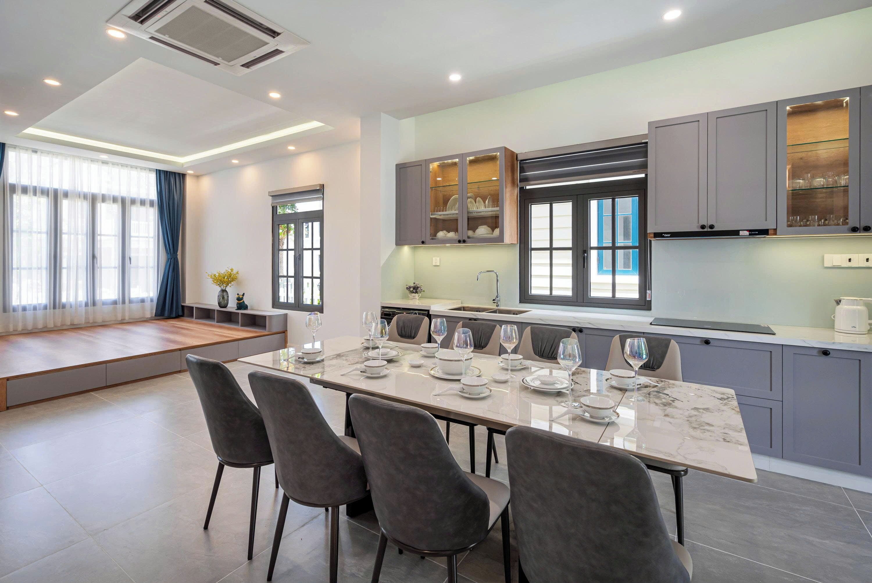 A modern kitchen with a large island, grey cabinets, and a seating area with a bench.