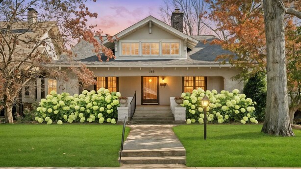 A two-story house with a front porch, a visible number '119', and a well-maintained lawn with large hydrangea bushes. - Hot Tub | Firepit | Putting Green | 5 Bedrooms (Shelbyville)