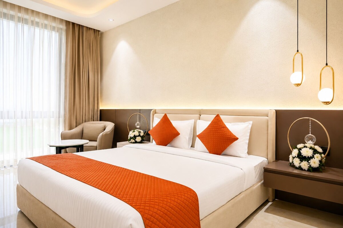 A hotel room with a large bed, a chair, a bedside table with a vase of flowers, and a view of the outdoors.