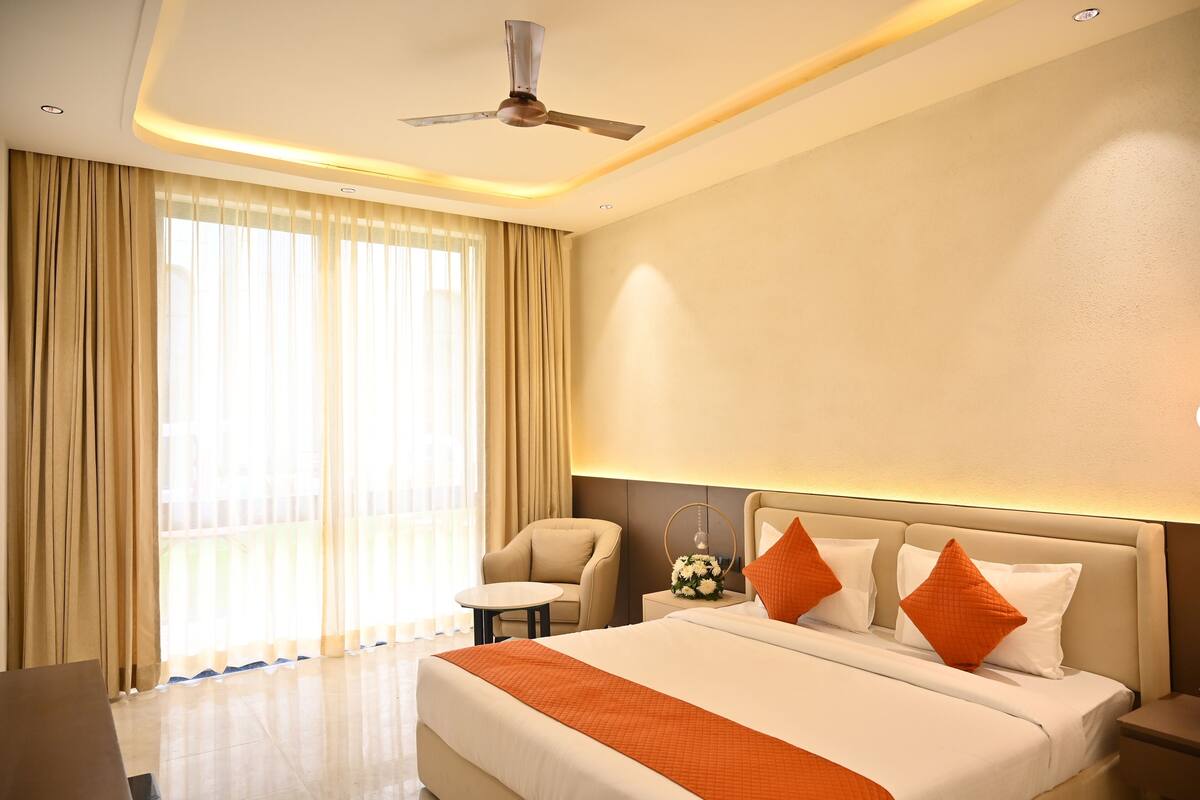 Habitación de hotel con cama, una silla, una mesita y un ventilador de techo.