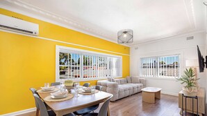 A dining area with a wooden table set for four, a sofa, and a small round table. - MetaWiseBnB | Cozy 2Bed Earlwood Near City&Airport (Earlwood)