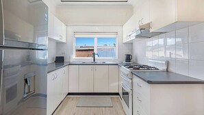 A modern kitchen with stainless steel appliances, white cabinetry, and a window providing a view. - MetaWiseBnB | Cozy 2Bed Earlwood Near City&Airport (Earlwood)