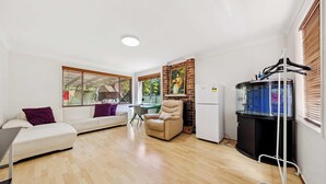 A modern living room with a sofa, armchair, and a dining table. There is a refrigerator, a water heater, and a window with blinds. - MetaWise Cozy Family Room4 in Shared Home Free Parking (Castle Hill)