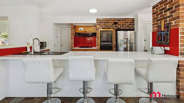 A modern kitchen with a white countertop, red accents, and a brick wall. - MetaWise Cozy Family Room4 in Shared Home Free Parking (Castle Hill)