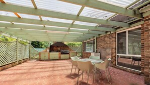 An outdoor patio with a brick barbecue area, a table with chairs, and a covered section with a metal roof. - MetaWise Cozy Family Room4 in Shared Home Free Parking (Castle Hill)