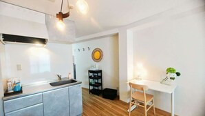 A modern kitchen with a built-in sink, a dining area with a white table and chair, and a small shelf with decorative items. - Sidihome 365 Apartment (Osaka)