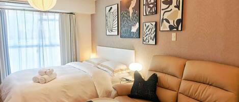 A hotel room with a bed, a sofa, a bedside table, and wall art.
