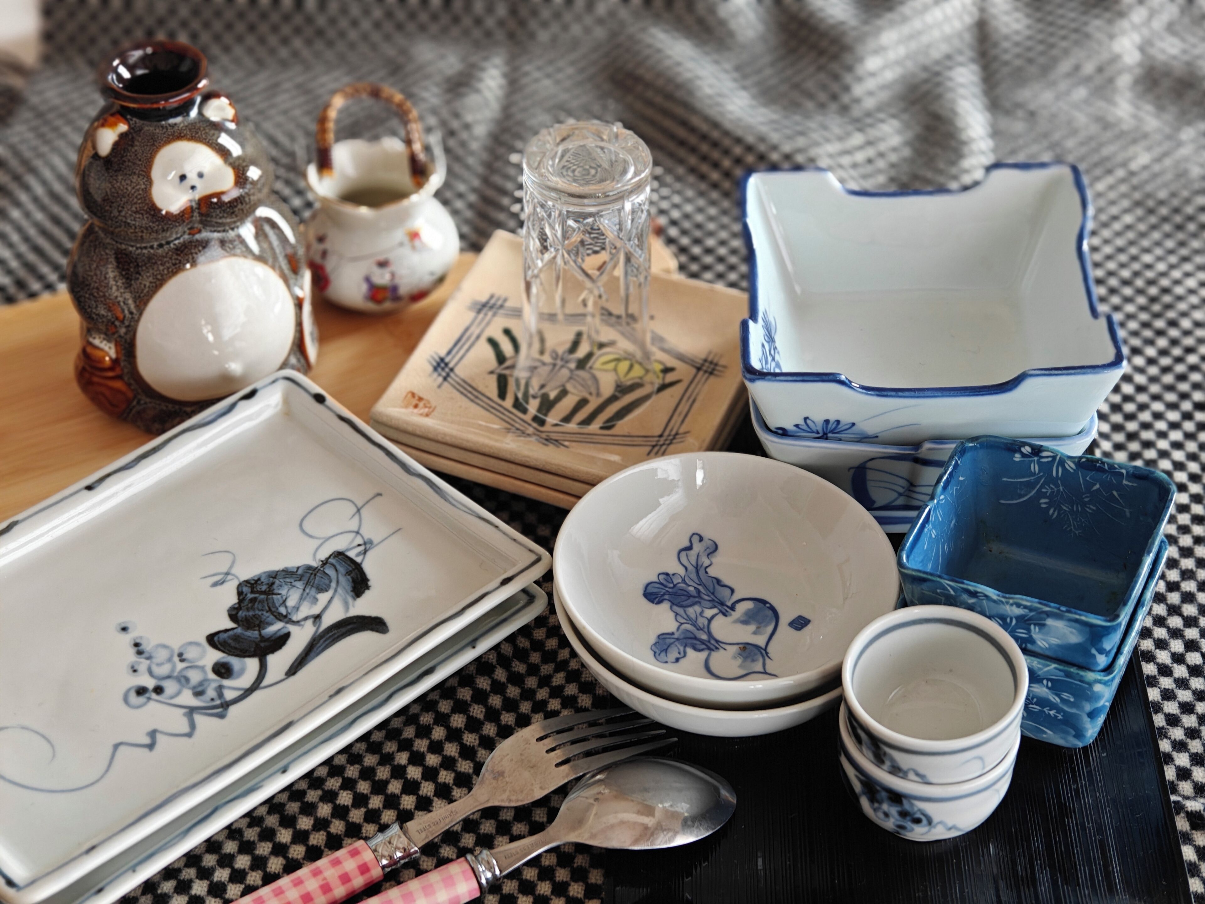 A variety of ceramic dishes and utensils on a checkered tablecloth.