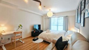 Una habitación de hotel moderna con una cama, un sofá, un escritorio con silla, un televisor y una ventana con cortinas.