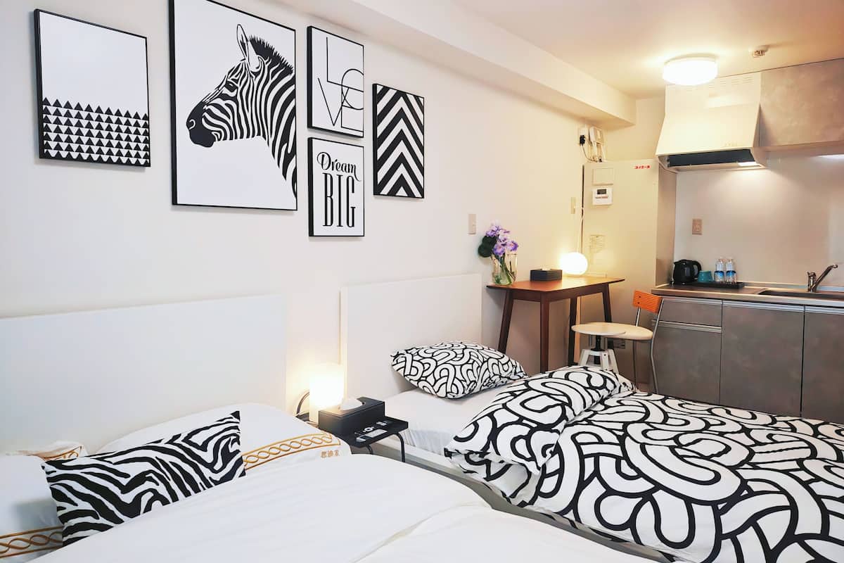Ein Hotelzimmer mit einem Bett, einem Nachttisch mit Lampe, einem kleinen Tisch mit Blumenvase und einer Küchenzeile.