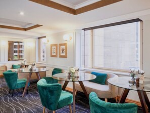 A hotel room with a seating area featuring round tables and teal chairs, a large window with a view, and a wall with framed artwork. - Fantastic city-view home in the Rocks (The Rocks)