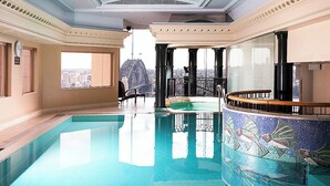 An indoor swimming pool with a view of a cityscape, a sunlit room with a large window, and a decorative mosaic pool edge. - Fantastic city-view home in the Rocks (The Rocks)