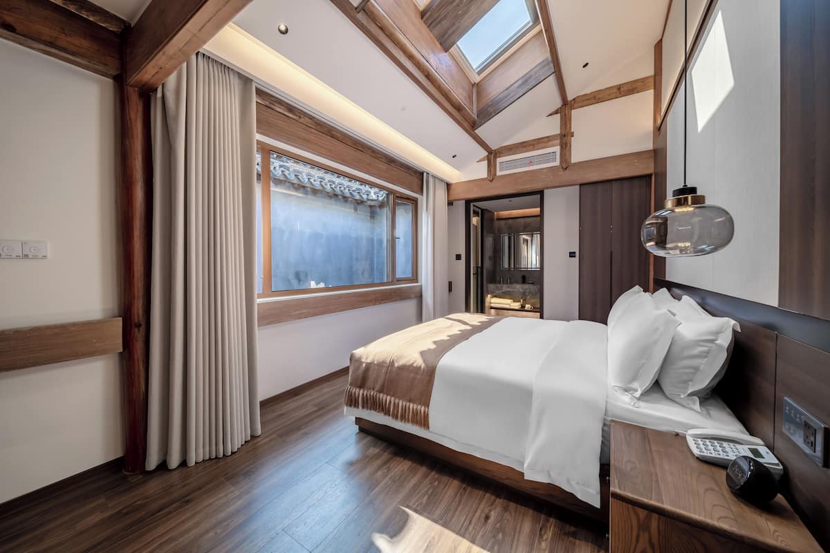 A modern hotel room with a large bed, wooden beams, a skylight, and a bedside telephone.