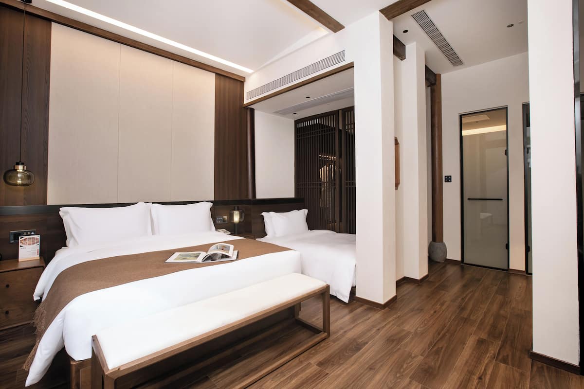 A hotel room with a large bed, a bench, a bedside table, and a wardrobe.