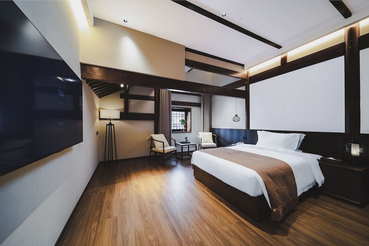 A modern hotel room with a large bed, a desk, a chair, a TV, and a window with curtains.