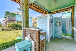 A covered outdoor area with a wooden bench, a sign indicating showers, and a lifebuoy on the wall. - Life`s better Salty - welcome to Serenity! (Bolivar Peninsula)