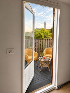 An open sliding door leading to a balcony with wicker chairs, a small round table, and a view of a tower in the distance. - Perfectly Situated: Downtown Luxury Loft (Reykjavík)